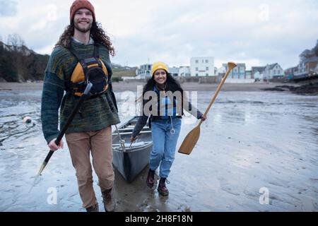 Un jeune couple heureux tirant en canoë sur une plage de sable humide Banque D'Images