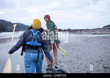 Jeune couple avec des oars tirant en canoë sur la plage Banque D'Images