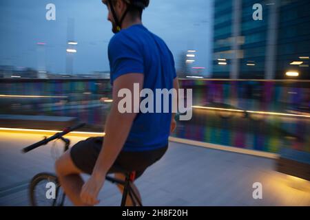 Homme à vélo sur une passerelle urbaine éclairée Banque D'Images
