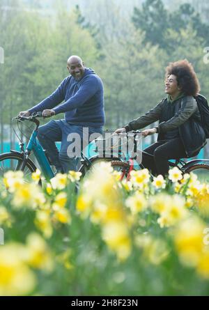 Un père heureux et un fils adolescent à vélo dans le parc de printemps Banque D'Images