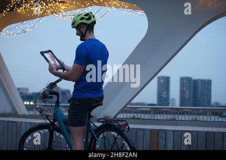 Homme à vélo, chat vidéo avec une tablette numérique dans la ville la nuit Banque D'Images
