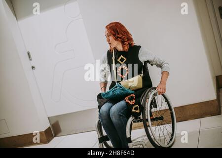 Une femme en fauteuil roulant près de la porte des toilettes avec un panneau de toilettes pour les personnes handicapées.toilettes publiques dans le centre commercial accessibles aux personnes o Banque D'Images