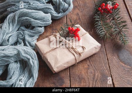 Boîte cadeau à côté de la nappe vintage gris et feuilles d'arbre de noël avec baies rouges sur une table en bois brun, composition festive sur un arrière-grou naturel Banque D'Images