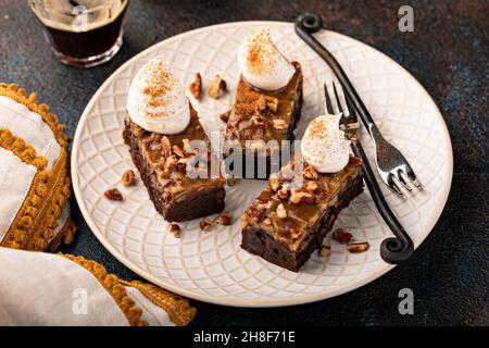 Barres de brownie à tarte aux noix de pécan assaisonnées de sauce caramel et servies avec de la crème fouettée saupoudrée de cannelle Banque D'Images