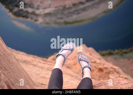 Les pieds de la femme qui pendent de la falaise à Horseshoe Bend, Arizona, portent des sandales Teva Banque D'Images