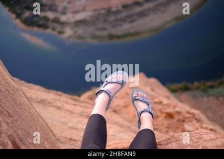 Les pieds de la femme qui pendent de la falaise à Horseshoe Bend, Arizona, portent des sandales Teva Banque D'Images