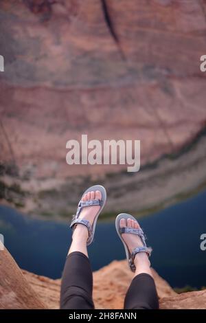 Les pieds de la femme qui pendent de la falaise à Horseshoe Bend, Arizona, portent des sandales Teva Banque D'Images