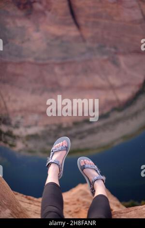 Les pieds de la femme qui pendent de la falaise à Horseshoe Bend, Arizona, portent des sandales Teva Banque D'Images