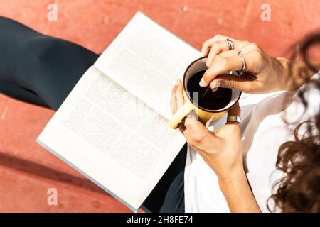 Détail des mains d'une femme lisant un livre tout en ayant un café le matin sur le toit Banque D'Images