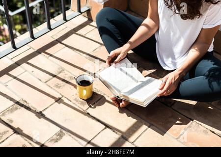 Jeune femme lisant un livre le matin tout en prenant un café sur le toit Banque D'Images