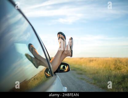 Fille qui colle ses pieds dans des tongs hors d'une fenêtre de voiture. Banque D'Images