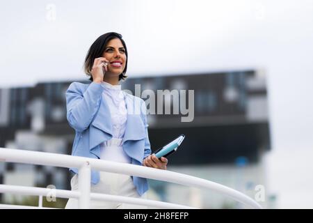Une femme d'affaires qui a du succès parle sur son spartphone dans la rue et tient une tablette Banque D'Images