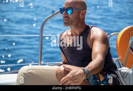 Portrait d'un beau homme portant des lunettes de soleil se détendant sur le Voilier.Vacances d'été sur le transport par eau.Voyage de luxe en Grèce.Europe. Banque D'Images