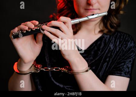 Femme musicienne avec une flûte aux mains menottées sur un fond sombre de studio.Les problèmes de la comédie musicale aux concerts, le concept de non-liberté et a Banque D'Images