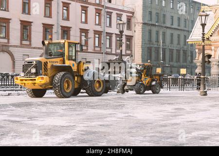 Saint-Pétersbourg, Russie - 16 janvier 2021 : le tracteur jaune Volvo et Wille déneigement la rue par temps sombre Banque D'Images