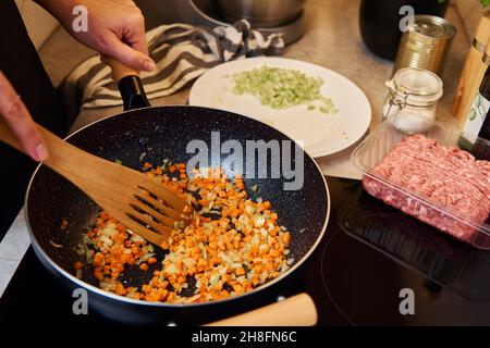 Femme cuisant de la sauce bolognaise dans une poêle à induction dans la cuisine Banque D'Images