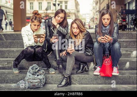 Groupe de filles assis sur les escaliers de la ville avec un smartphone.Isolement technologique et déprsion émotionnelle Banque D'Images