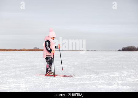 La petite fille apprend à skier.Enfant en costume rose chaud ski dans la neige par temps froid en hiver, vue latérale, fond de neige Banque D'Images