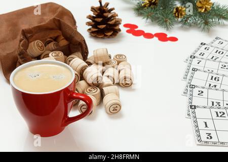 Lotto de jeu de société.Tasse de café, fûts de lotto en bois avec sac marron, cartes de jeu et jetons rouges.Branches de sapin de Noël sur le fond Banque D'Images