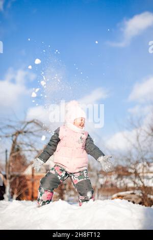 La fille joue des boules de neige contre le ciel bleu.Enfant en costume d'hiver chaud a du plaisir, joue et saute sur les snowdrifts, manèges de neige tout en marchant dans la nature Banque D'Images