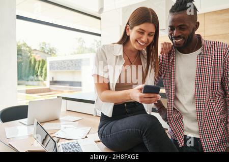 Une femme pleine d'esprit qui montre quelque chose sur son smartphone à un homme heureux Banque D'Images
