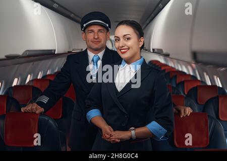 Hôtesse d'avion souriante et capitaine debout dans l'allée Banque D'Images