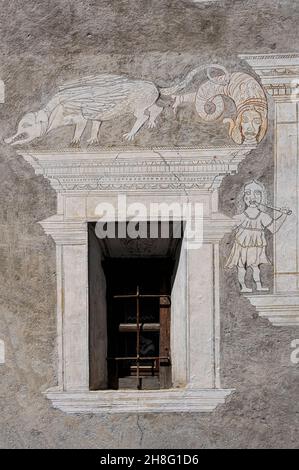 Un animal hybride bizarre avec des dents de crocodile, des ailes et une queue écailleuse partage le haut d'une fenêtre avec un monstre marin avec un visage humain, comme une fille avec de longs cheveux souffle une corne ou un tuyau:L'art sgraffito rustique, charmant mais hors-la-vue, se trouve à l'avant d'une maison familiale traditionnelle dans le canton d'Ardez, des Grisons ou des Grisons, dans l'est de la Suisse.La façade restaurée, datée de 1665, comporte également une inscription en langue romanche. Banque D'Images