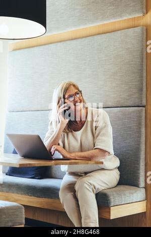 Femme d'affaires gaie et mûre parlant au téléphone.Bonne femme d'affaires mûre souriant dans un espace de travail moderne.Entrée expérimentée Banque D'Images