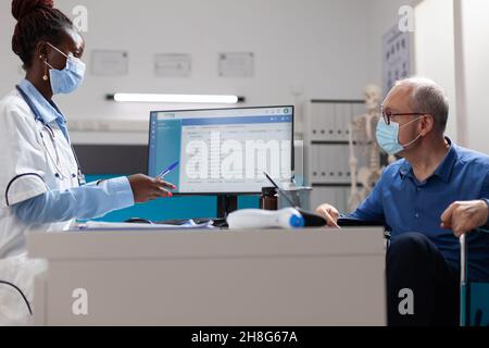 Médecin médecin médecin portant un masque de protection pour prévenir l'infection cu covid19 discuter de l'expertise de la maladie avec un homme âgé en fauteuil roulant pendant un rendez-vous médical dans le bureau de l'hôpital.Concept de médecine Banque D'Images