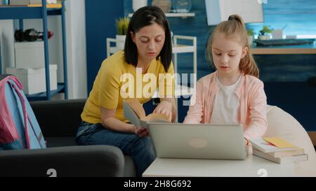 Mère et fille lisant le livre ensemble et faisant leurs devoirs à la maison.Écolière recevant l'hépatite d'un parent avec des cours et des tâches en ligne pour l'éducation à distance.Adulte aidant l'enfant Banque D'Images