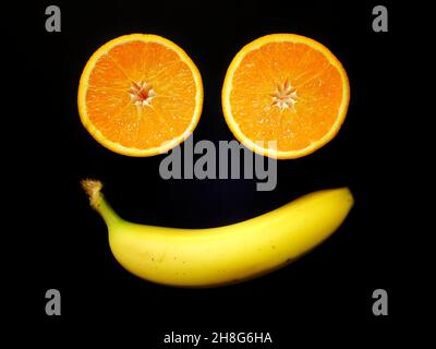 Simple visage de fruit fait de banane et deux moitiés orange sur fond noir Banque D'Images