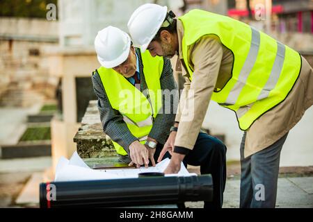 Deux ouvriers de la construction regardent les plans sur le papier tout en ayant une conversation, gros plan Banque D'Images