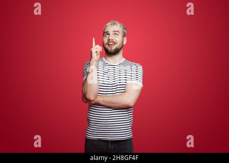 Homme caucasien portant un t-shirt rayé debout sur un arrière-plan rose isolé souriant et pointant vers le haut avec l'index. Banque D'Images