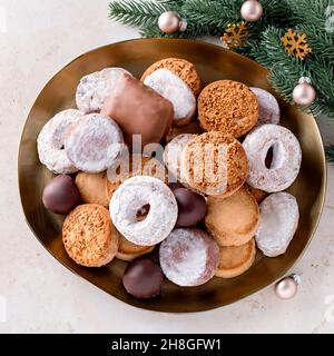 Les délices des fêtes polvorones et les mantecados en assiette dorée sur une table en pierre beige décorée de boules dorées, de branches d'arbre de noël et de cône de pin Banque D'Images