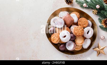 Les délices des fêtes polvorones et les mantecados en assiette dorée sur une table en pierre beige décorée de boules dorées, de branches d'arbre de noël et de cône de pin Banque D'Images