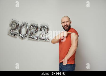 Un homme chauve avec une barbe crie et montre un plâtre médical sur son épaule après la vaccination contre le coronavirus (Covid-19) près de l'argent moussé Banque D'Images