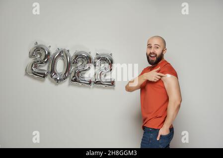 Un homme chauve souriant avec une barbe crie et montre un plâtre médical sur son épaule après la vaccination contre le coronavirus (Covid-19) près de la pouille Banque D'Images