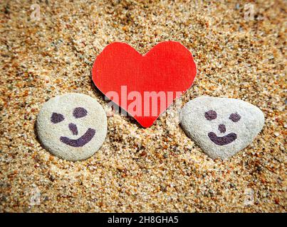 Des visages Smiley peints sur les galets et la forme de coeur dans le sable Banque D'Images