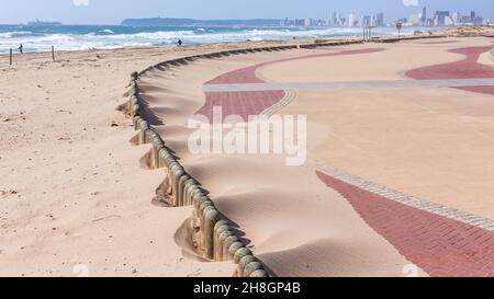 Le sable qui se déplace sur la plage souffle sur des rôles en bois peu élevés sur la promenade en tas de grain pendant la saison des vents forts. Banque D'Images