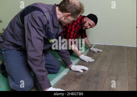 Un travailleur frappe les mains sur un stratifié reliant les panneaux par un clic de verrouillage Banque D'Images