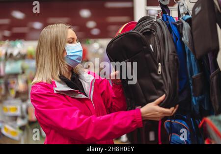 Femme dans le masque médical est de choisir le sac à dos pour enfant pour l'école. Banque D'Images