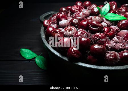 Beaucoup de cerise surgelée sans bâtons dans le bol avec des feuilles vertes sur un fond noir en bois.vitamines et une alimentation saine Banque D'Images