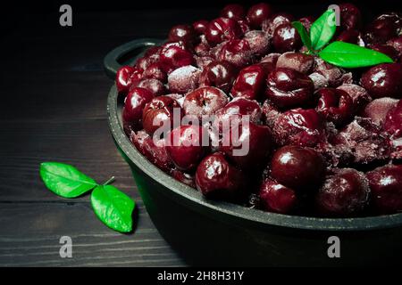 Beaucoup de cerise surgelée sans bâtons dans le bol avec des feuilles vertes sur un fond noir en bois.vitamines et une alimentation saine Banque D'Images