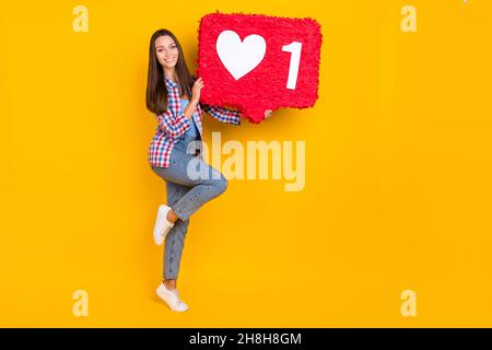 Photo de la femme insouciante funky tenir rouge grand un coeur pinata porter chemise à carreaux isolé couleur jaune arrière-plan Banque D'Images