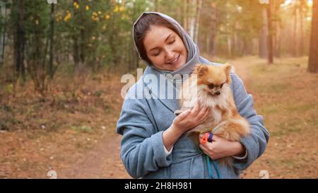 Jeune femme tenant le pomeranian mini spitz dans les bras tout en marchant dans le parc d'automne Banque D'Images