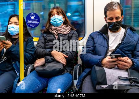 Passagers portant un masque facial sur Un train souterrain de Londres, Londres, Royaume-Uni. Banque D'Images