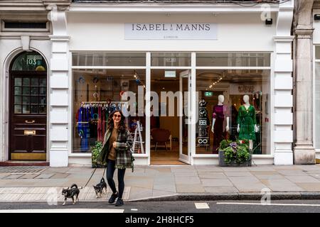 Une femme bien habillée passe ses chiens devant la boutique de vêtements pour femmes Isabel Manns, Marylebone High Street, Londres, Royaume-Uni. Banque D'Images