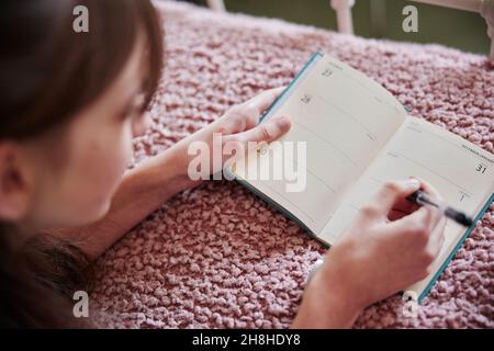 Adolescente couchée au lit à la maison écrivant des résolutions dans le journal du nouvel an ou journal Banque D'Images