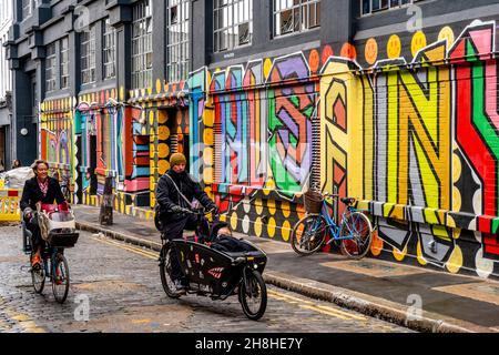 Deux personnes passant devant des graffitis colorés,/Street Art à Shoreditch, Londres, Royaume-Uni. Banque D'Images