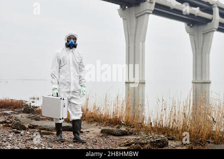 Portrait d'un travailleur portant un costume de noisette marchant dans l'eau à l'extérieur et transportant des échantillons mallette, concept de déchets industriels, espace de copie Banque D'Images